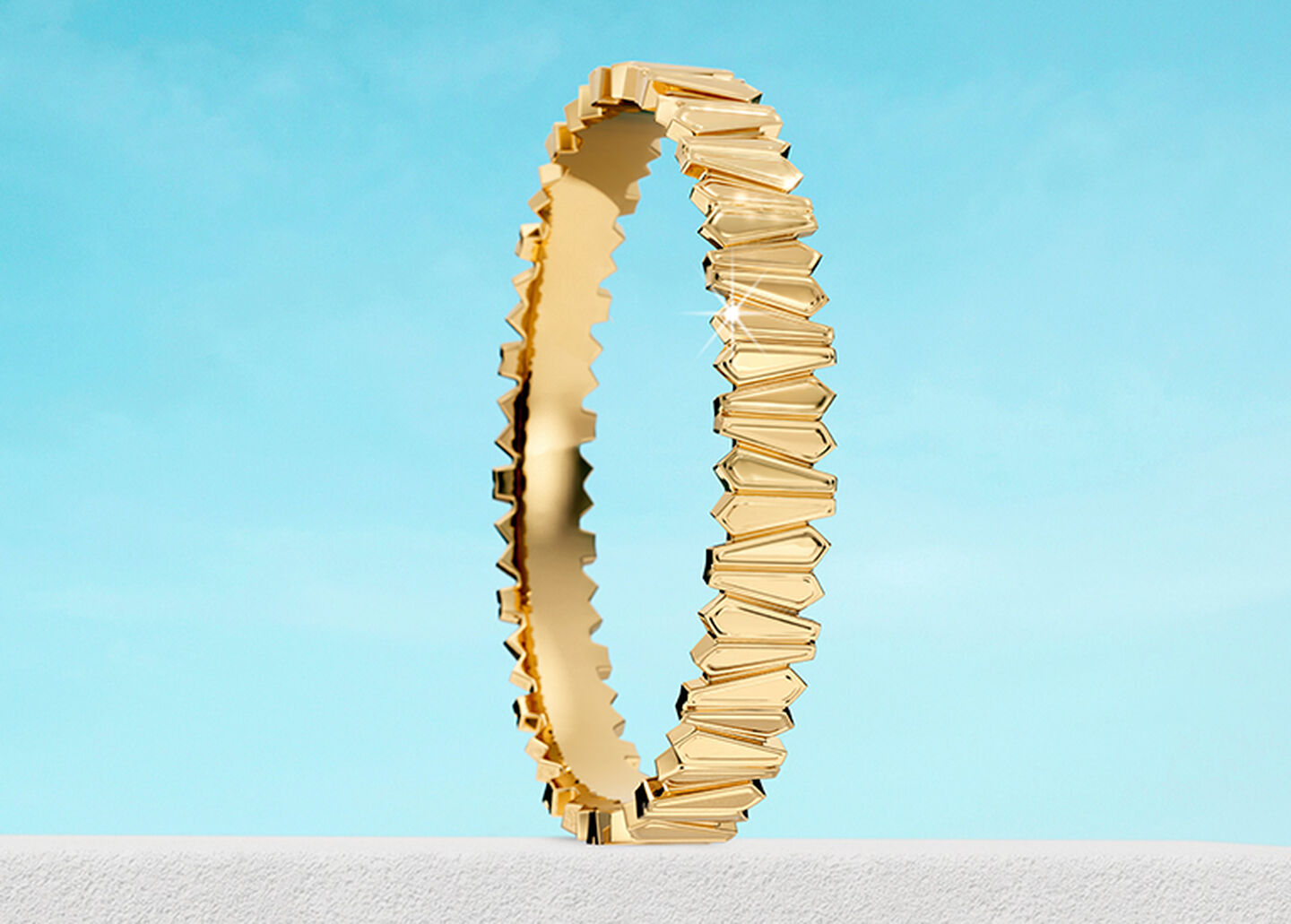 Bracelet jonc Birks Beekeeper en or jaune sur un fond de ciel.