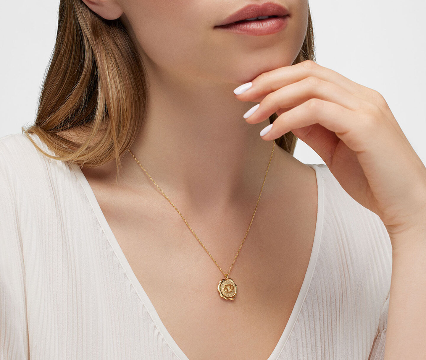 A woman wearing a Birks Essentials Zodiac Cancer necklace in yellow gold.