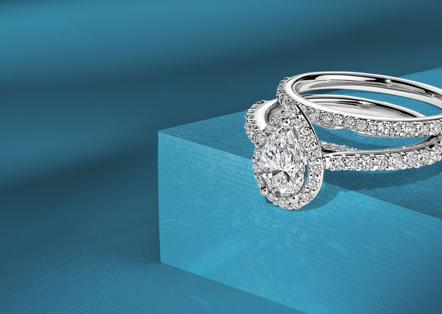 Bague de fian&ccedil;ailles solitaire diamant taille poire Birks avec anneau pav&eacute; et alliance assortie sertie de diamants en or rose sur fond bleu.