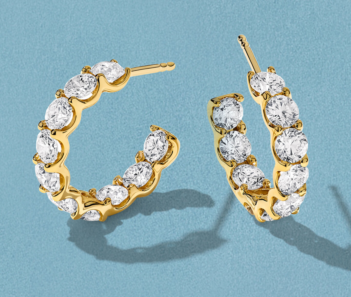 Boucles d'oreilles Birks Essentiels en or jaune avec diamants sur un fond bleu.
