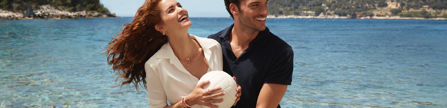A man and woman embracing on the beach wearing FRED jewellery.