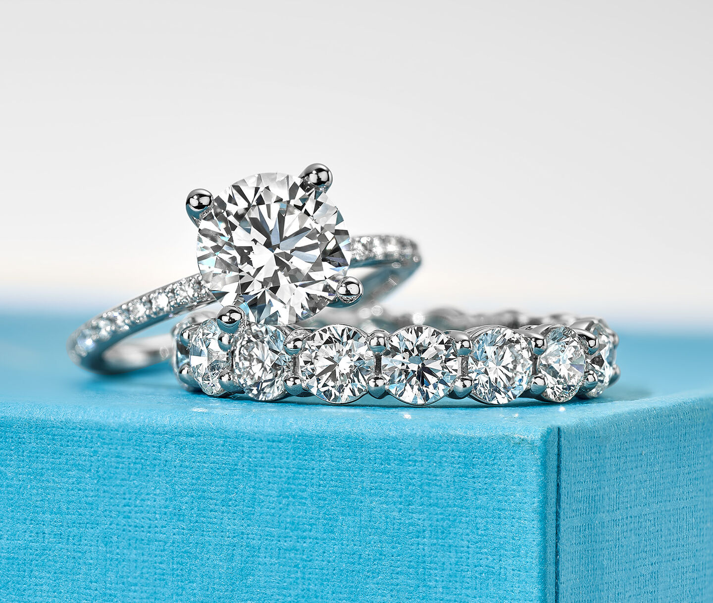 Une bague de fiançailles à diamant solitaire et bague éternité Birks sur une boîte bleue.