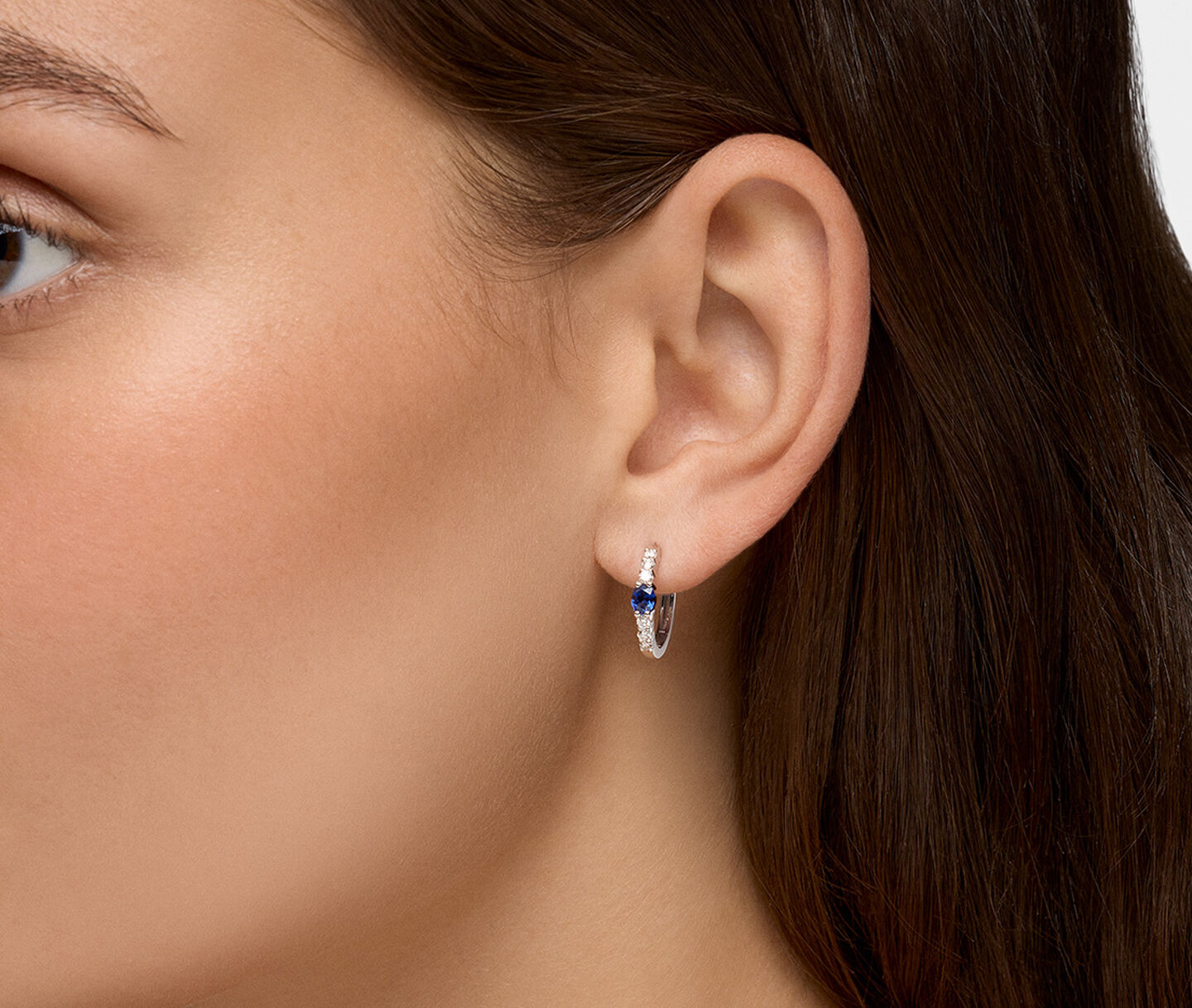 A woman wearing Birks Essentials sapphire and diamond hoop earrings.