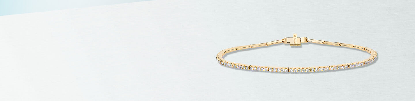 Bracelet Birks Essentiels avec diamants en or jaune sur un fond bleu.