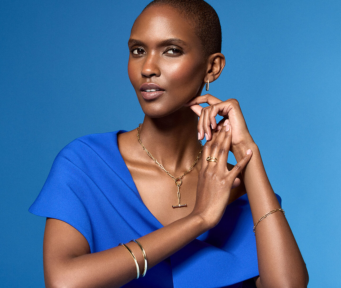 Une femme porte les bijoux en or jaune de Maison Birks sur un fond bleu.