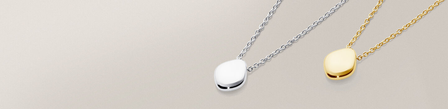 Pendentif en or jaune et argent Birks Pebble sur un fond tirant sur le gris et beige
