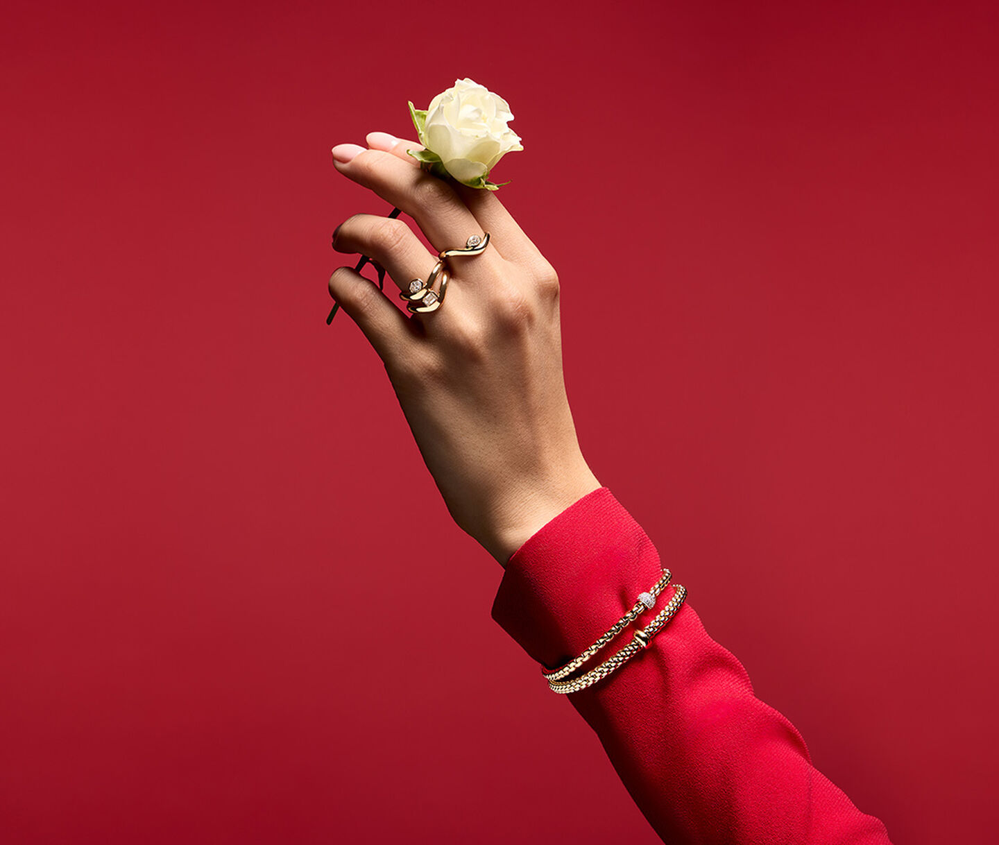 A woman holding a rose wearing Maison Birks jewellery on a red background.