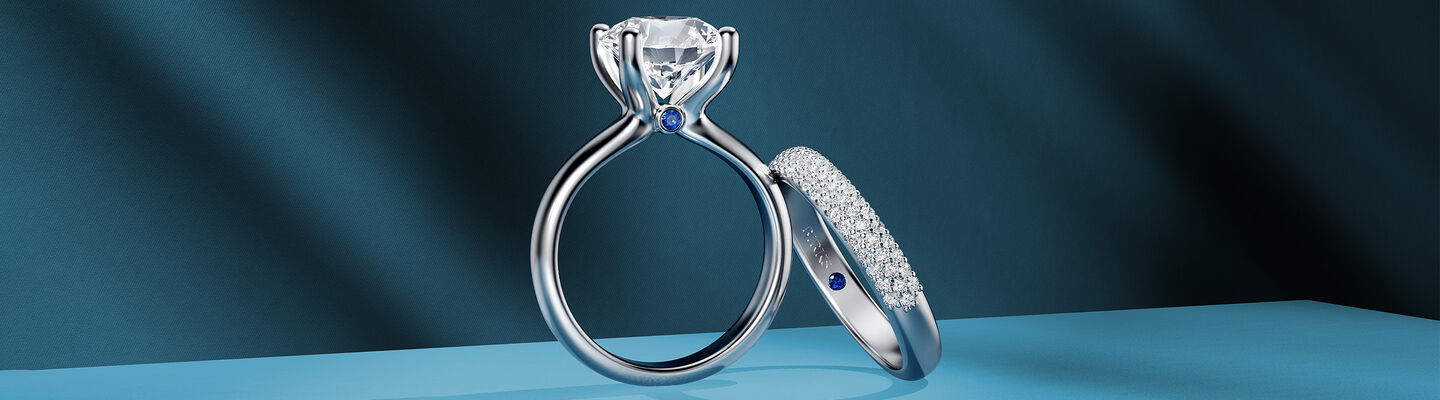 A Birks Blue engagement ring and diamond wedding band on a dark blue background.