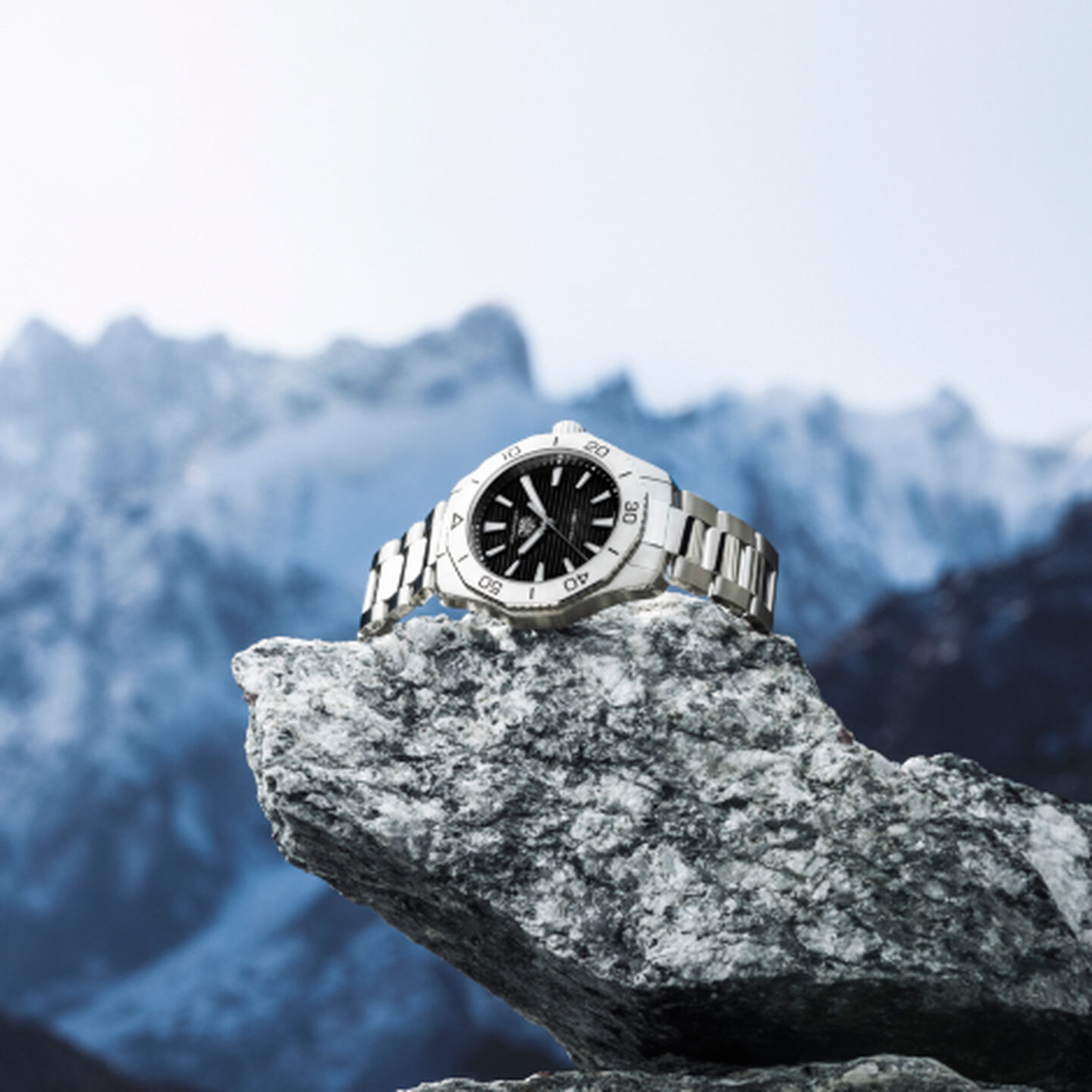 A TAG Heuer watch perched upon a rock overlooking snow covered mountains