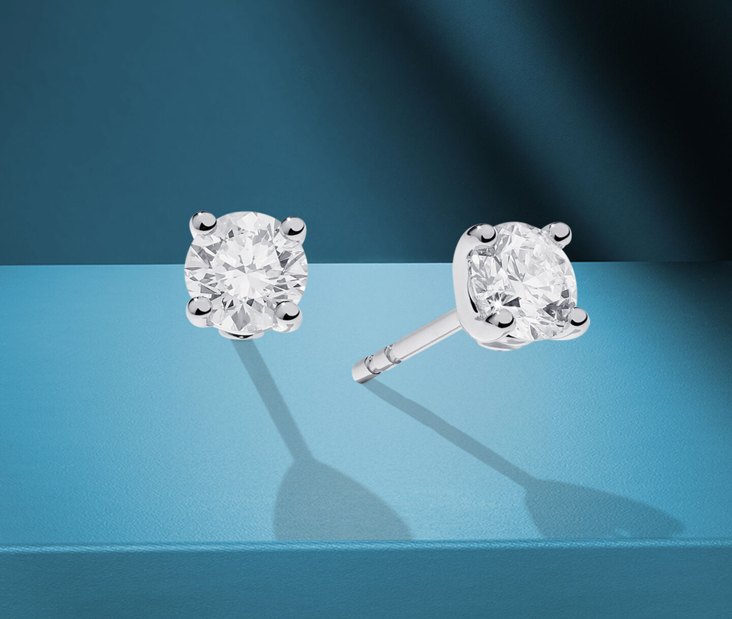 Birks solitaire diamond earrings on a blue background.