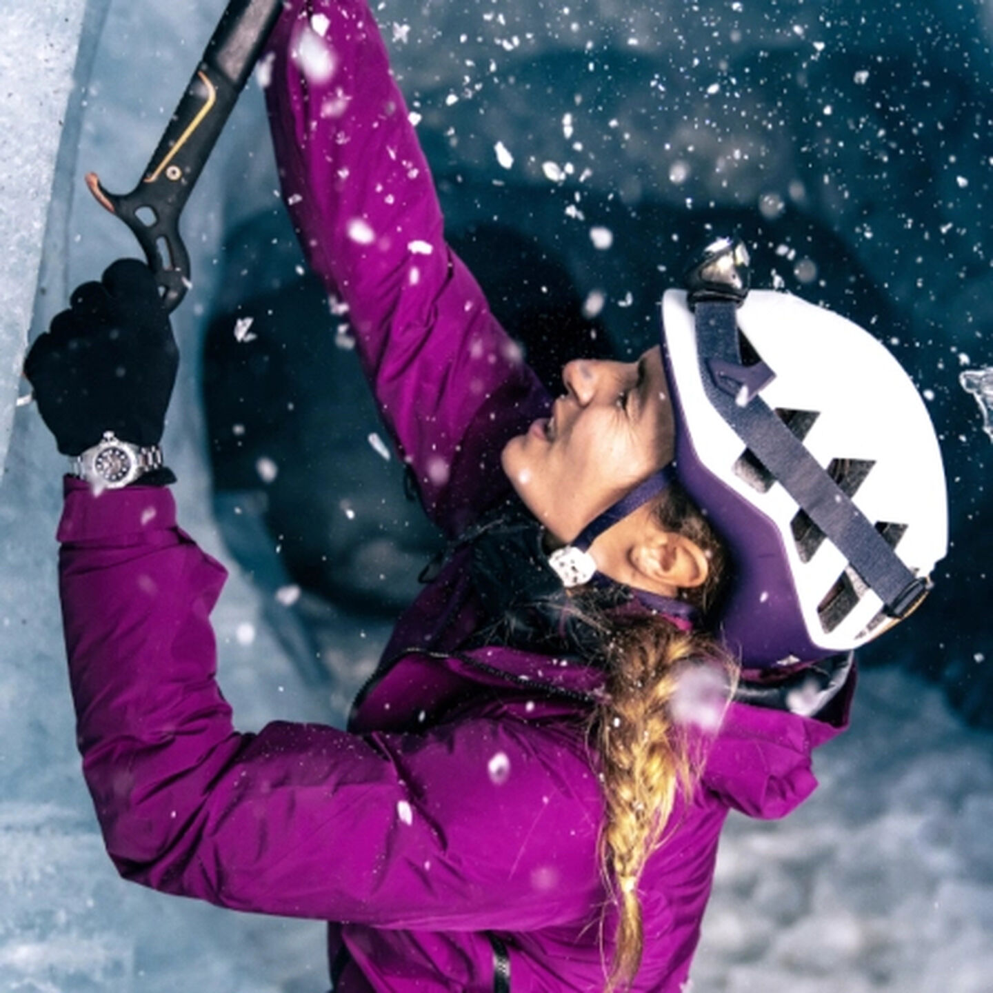 A woman ice climbing in a purple jacket and white helmet