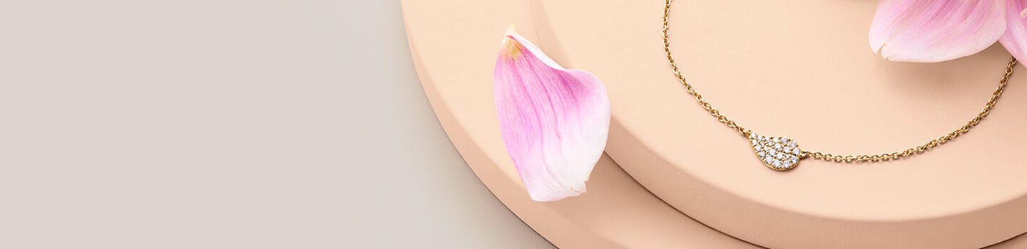 A gold necklace with a diamond Birks Pétale pendant surrounded by pink flower petals.