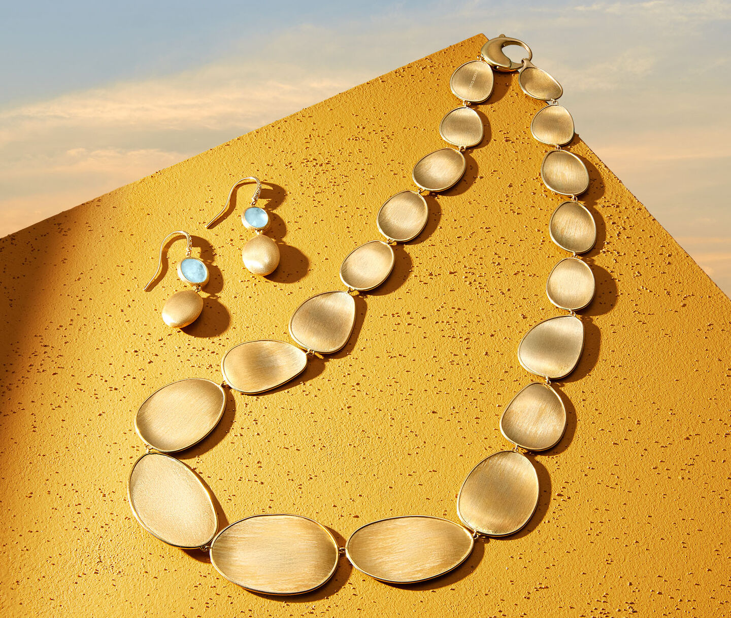 Marco Bicego Lunaria earrings and necklace on a gold background.