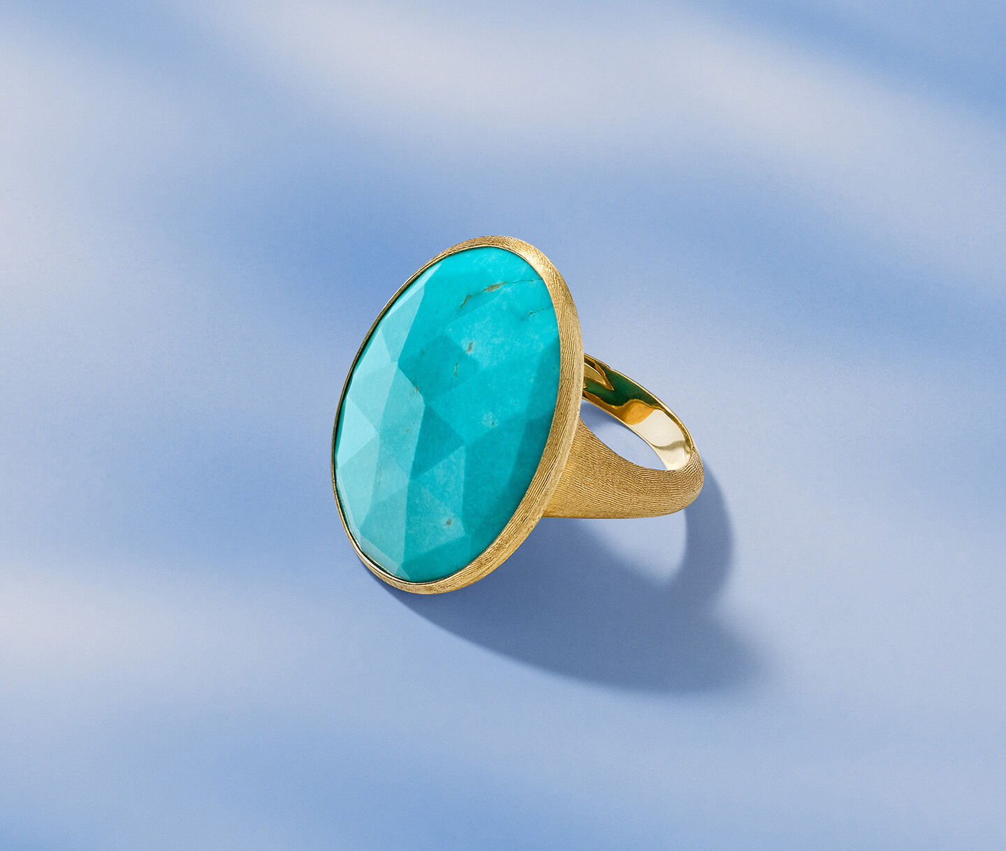 Marco Bicego yellow gold and turquoise ring on a blue background.