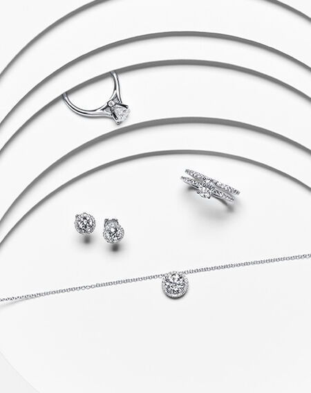 Two Birks diamond engagement rings and diamond earrings and necklace on a white layered background.