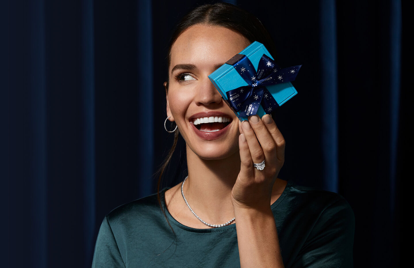 A model smiles while holding up a blue gift wrapped box