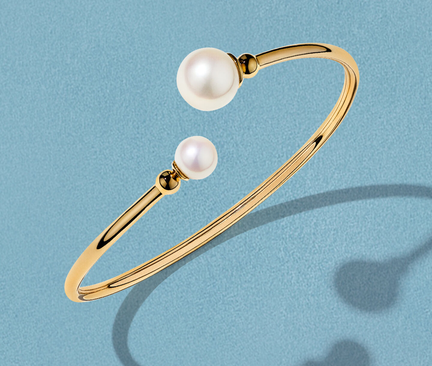 Bracelet Birks Essentiels en or jaune avec perles sur un fond bleu.