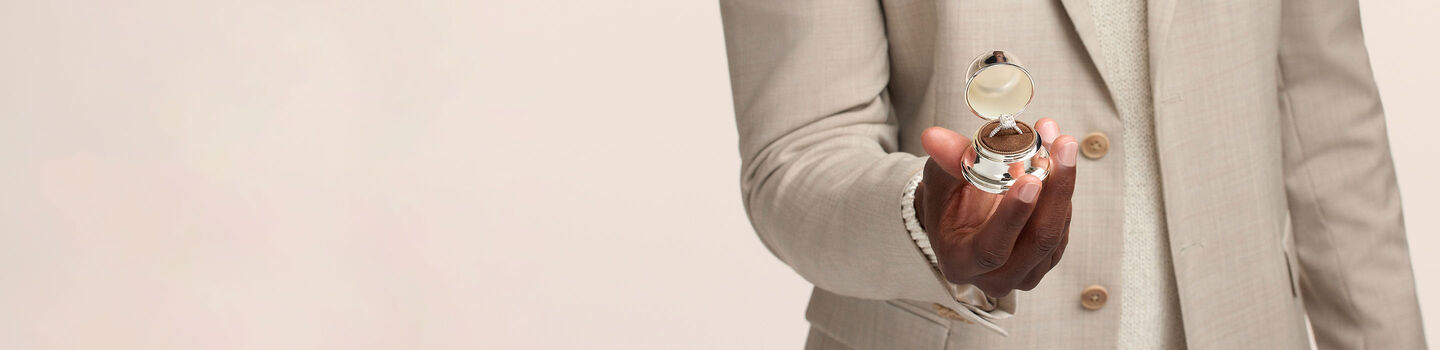 A man holding a Birks diamond engagement ring in it's Bell Box.