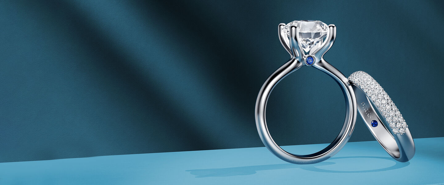 A Birks Blue diamond engagement ring and wedding band on a dark blue background.