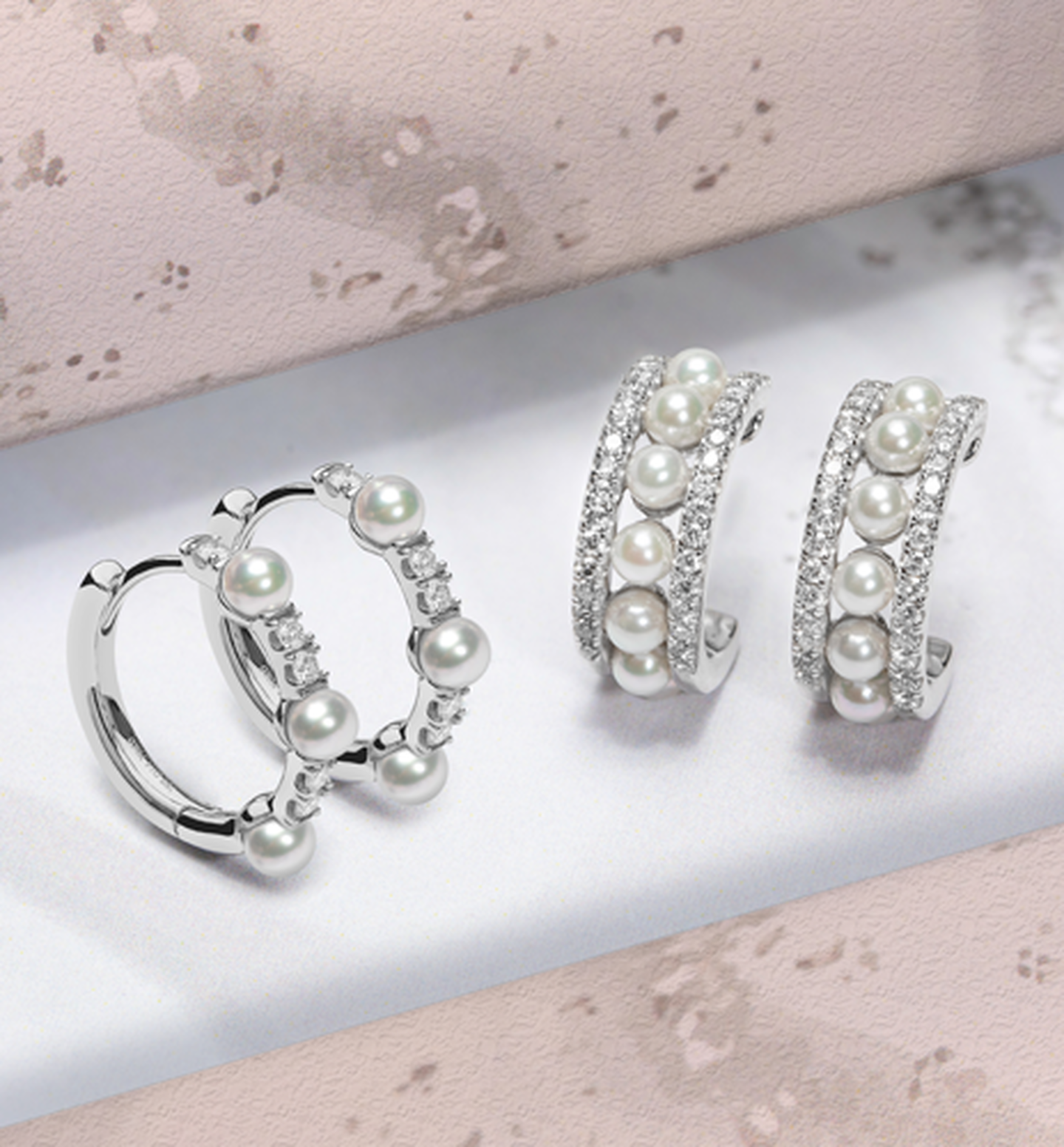 A box containing Yoko London pearl and diamond earrings rest on a pile of snow with a pink ribbon.