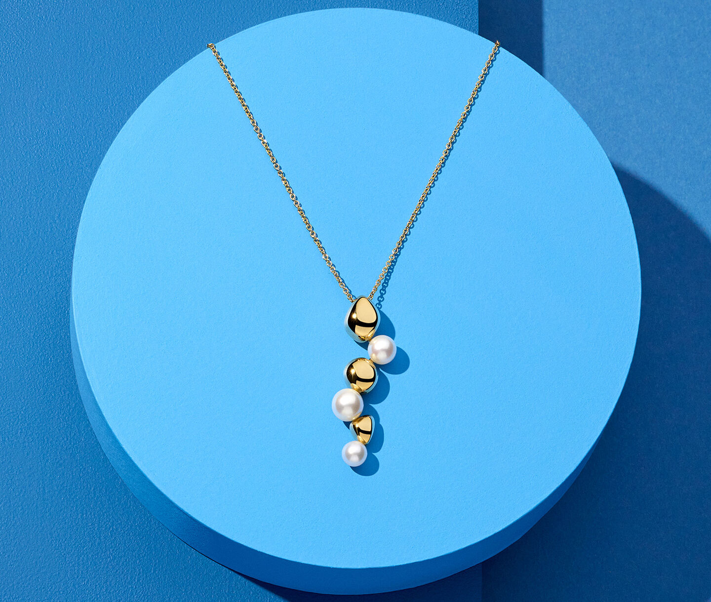 Birks Pebble yellow gold and pearl drop necklace on a blue background.
