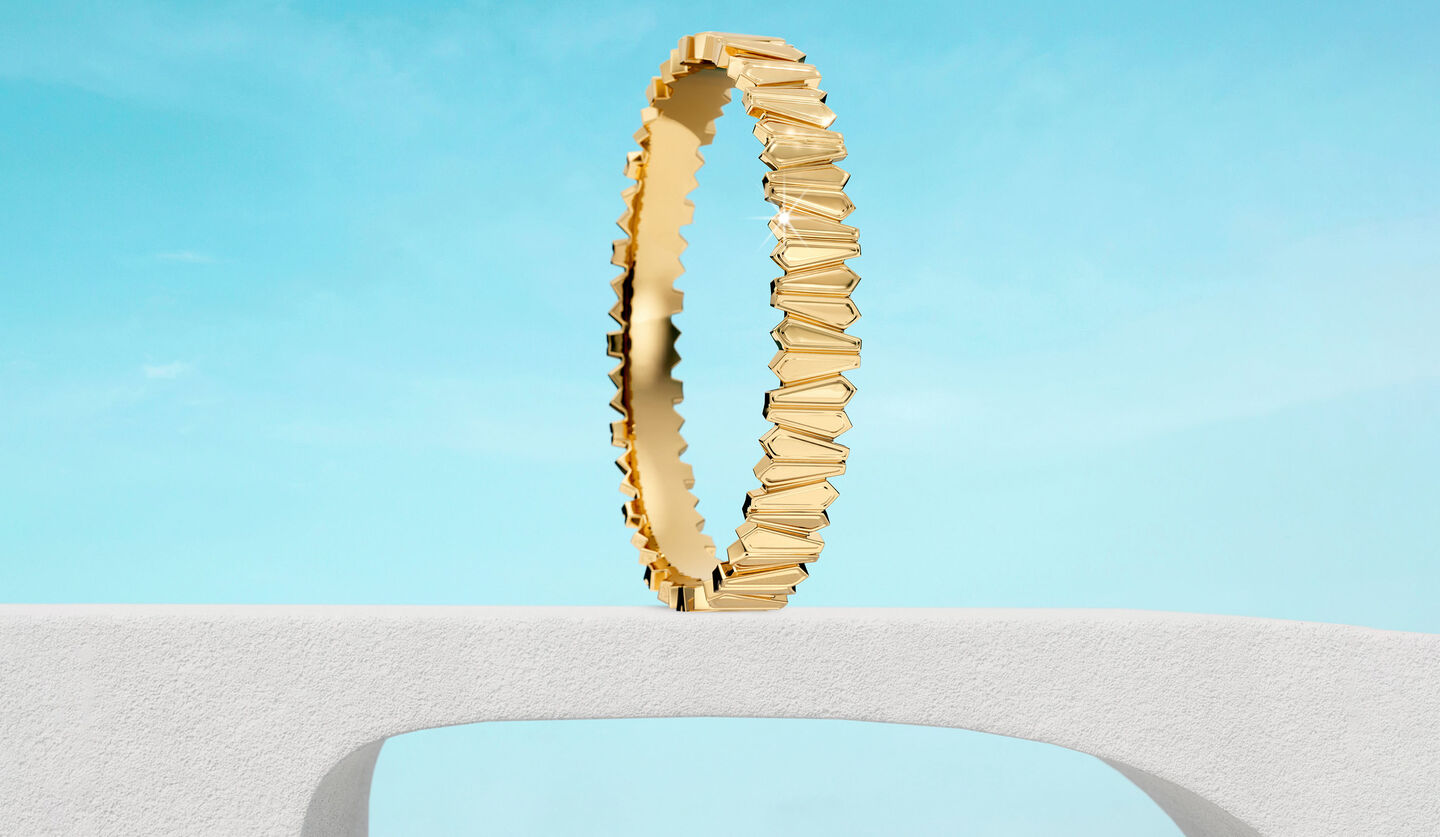 Birks Beekeeper yellow gold bangle bracelet on a sky background.