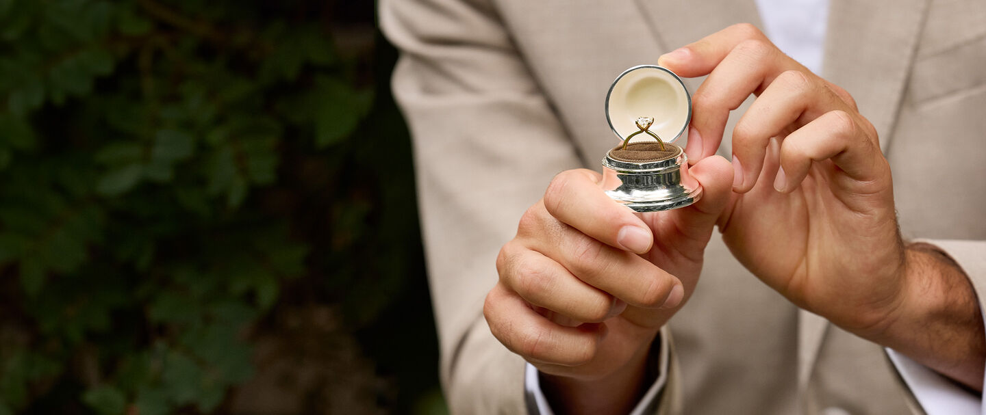 A man holding a Birks Bell Box with a diamond engagement ring.