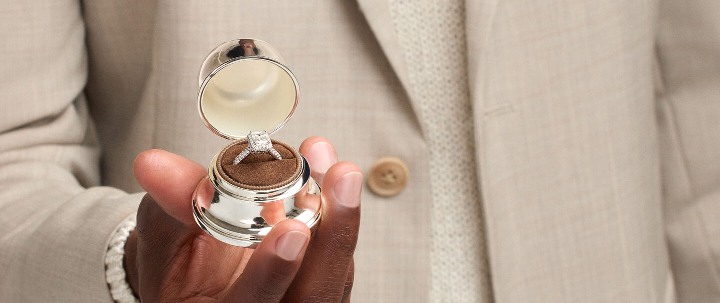 A man holding a Birks Bell Box with a diamond engagement ring.