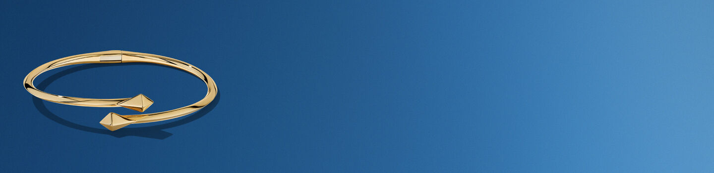 Birks Rock & Pearl yellow gold bracelet on a blue background.