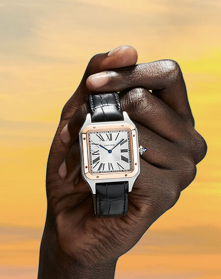 Un homme tient une montre Santos de Cartier avec un fond du ciel