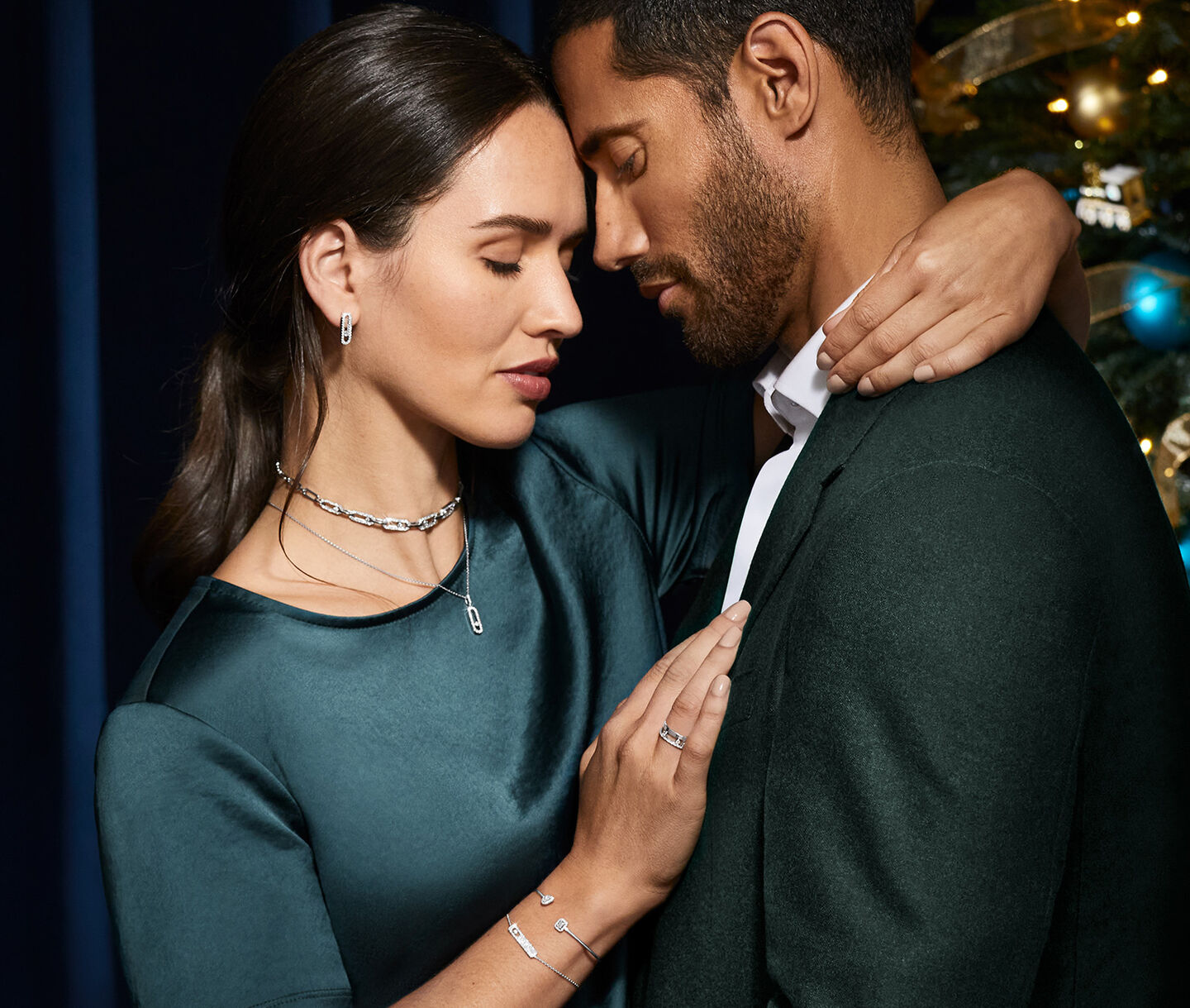 A man and woman wearing green and Messika diamonds lean into each other. 