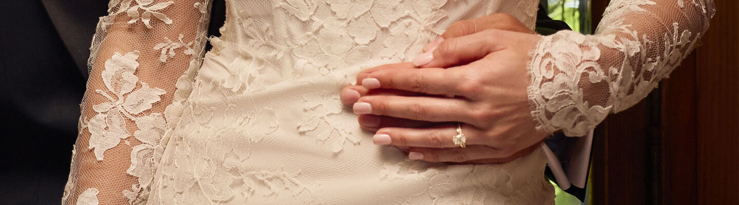 Close-up of a Birks diamond solitaire engagement ring on hand with lace wedding attire.