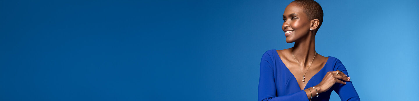 A woman wearing Birks Pebble yellow gold and pearl jewellery on a blue background.
