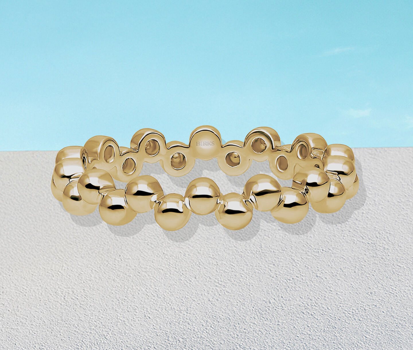 Birks Iconic Splash yellow gold ring on a blue background.