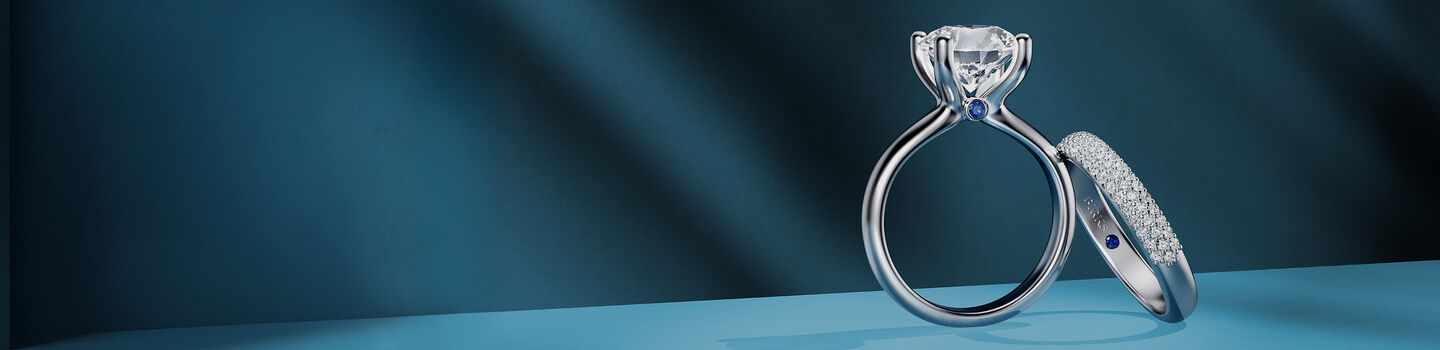 Birks Blue diamond engagement ring and wedding band on a blue background.