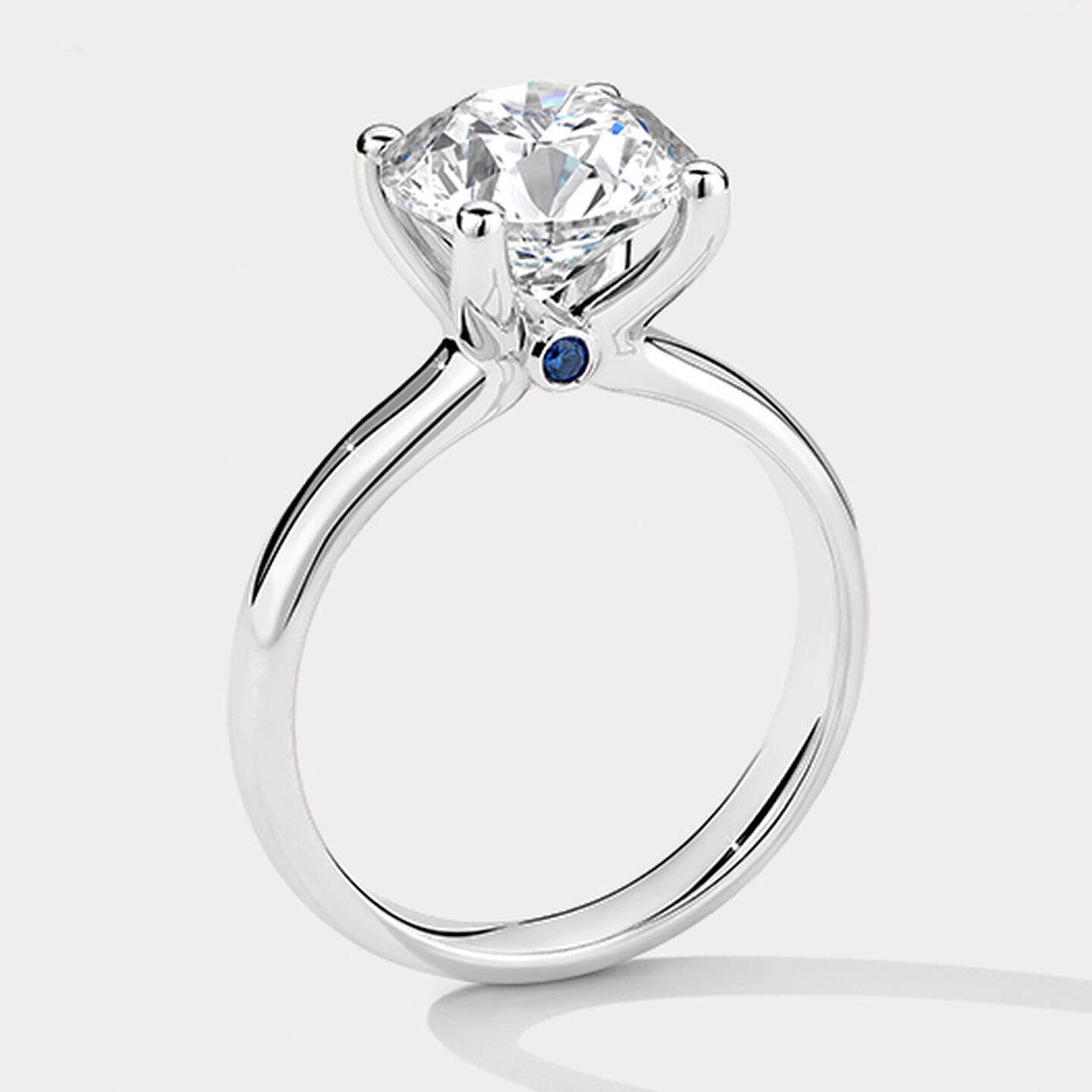 Birks Blue Diamond Engagement Ring with Sapphire Accent on a beige background.
