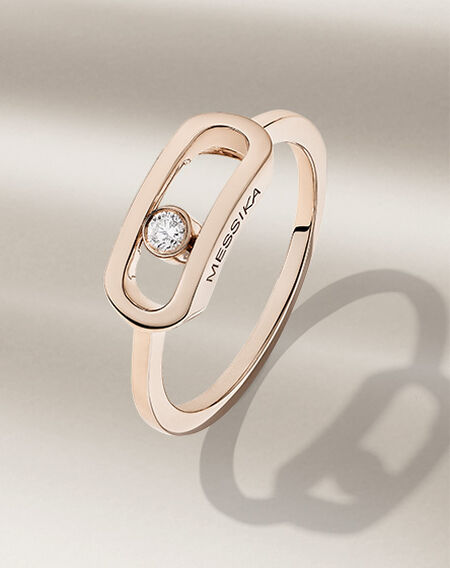 Bague en or rose avec diamant Messika sur un fond beige.