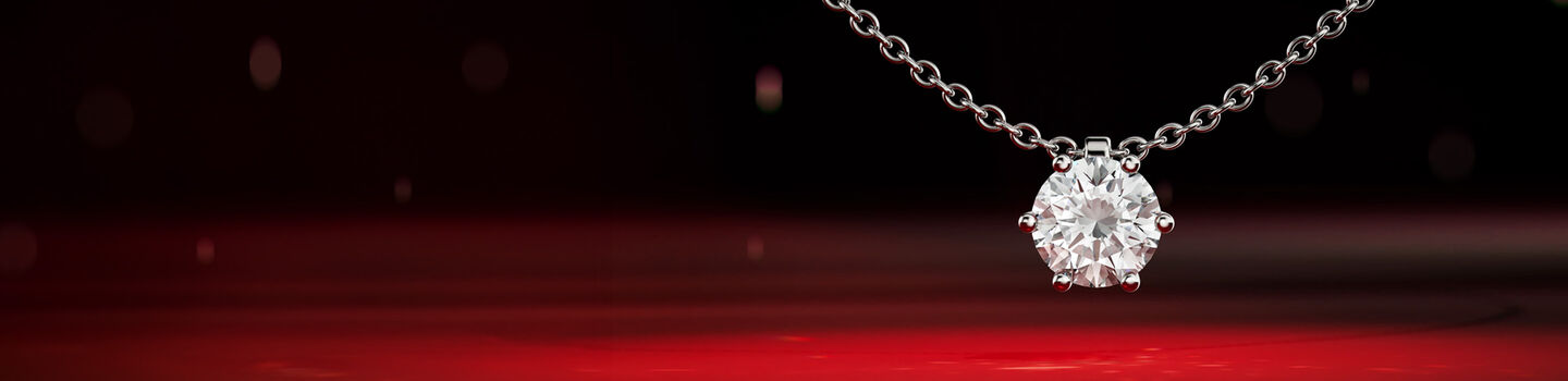 Maison Birks diamond solitaire pendant necklace on a red background.