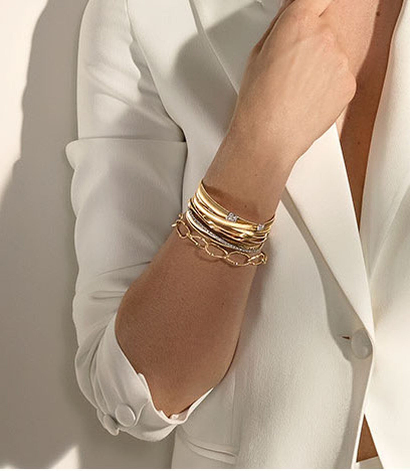 Model in a white blazer wearing gold Marco Bicego bracelets.