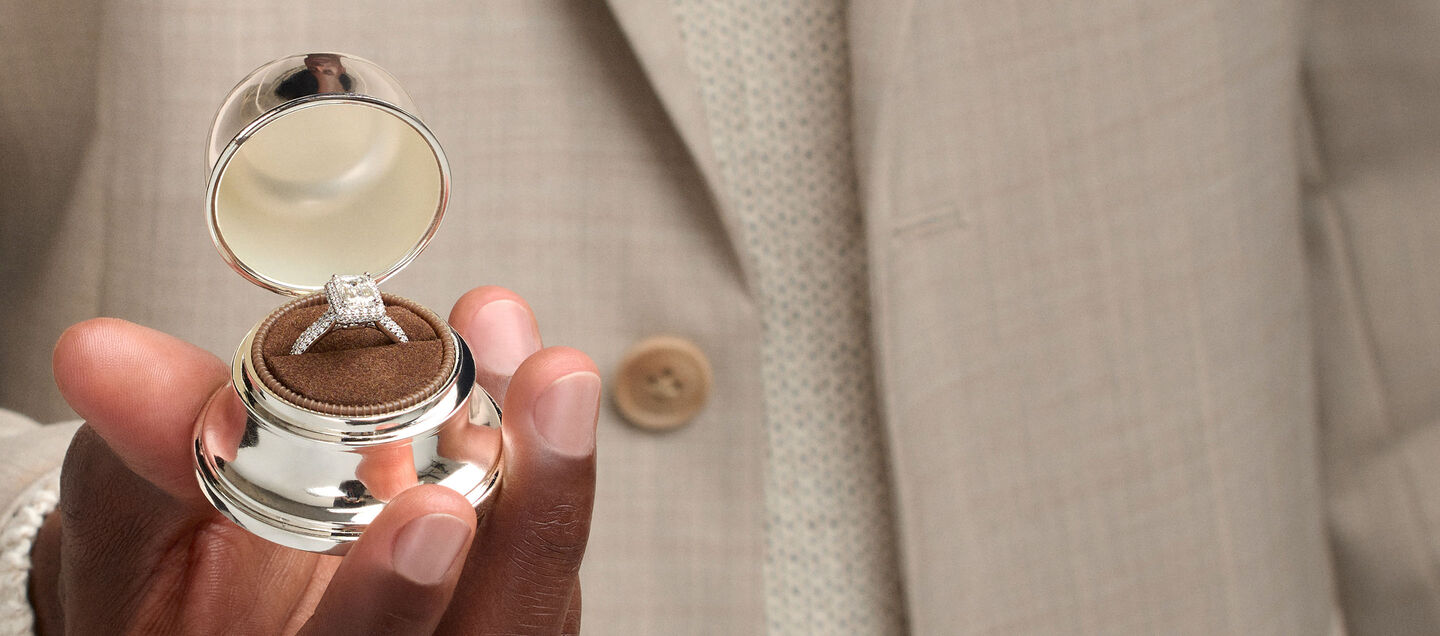 Un homme tenant une boîte de cloche Birks contenant une bague de fiançailles en diamant.