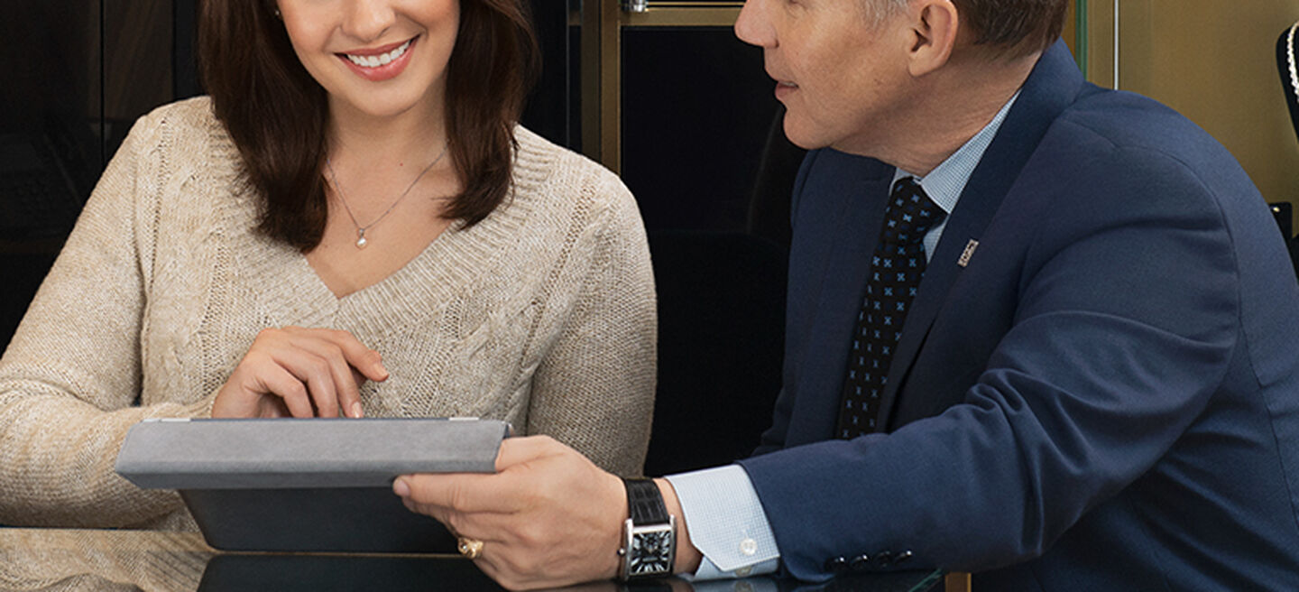 A man in a blue suit showing a woman in a tan sweater a tablet