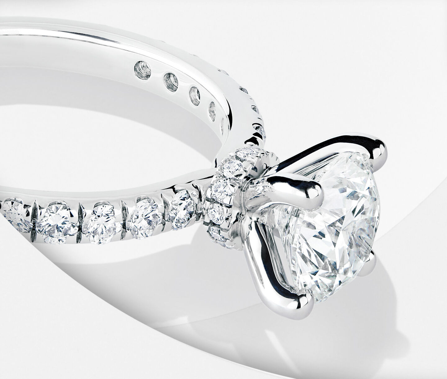 Bague de fiançailles à diamant solitaire rond avec anneau serti de diamants sur un fond blanc.