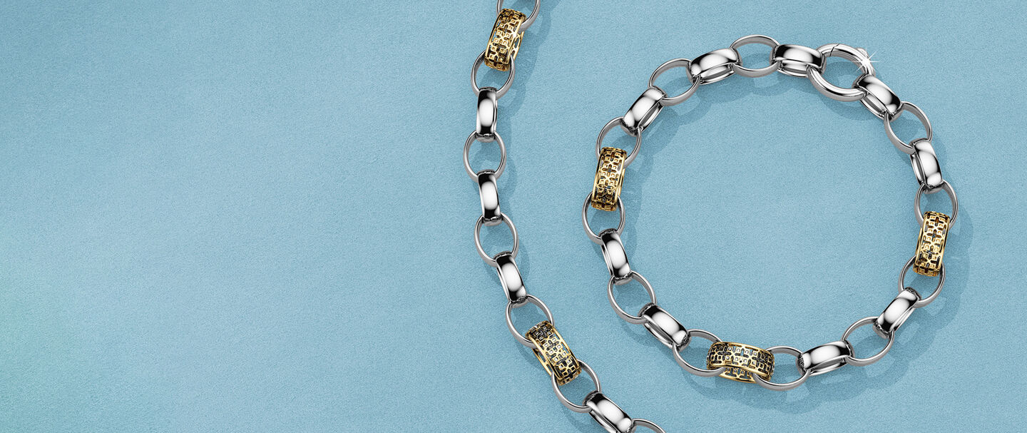Birks Dare to Dream silver and gold necklace and bracelet on a blue background.