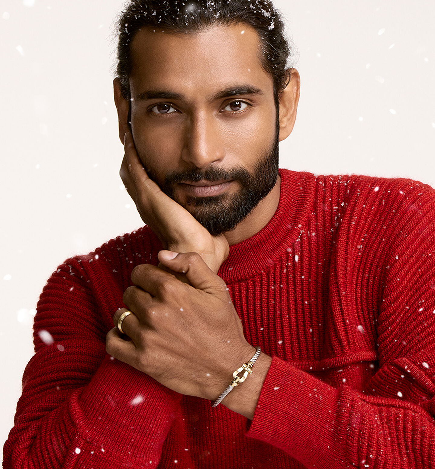 Person in red sweater wearing FRED bracelet with snowflakes falling around.