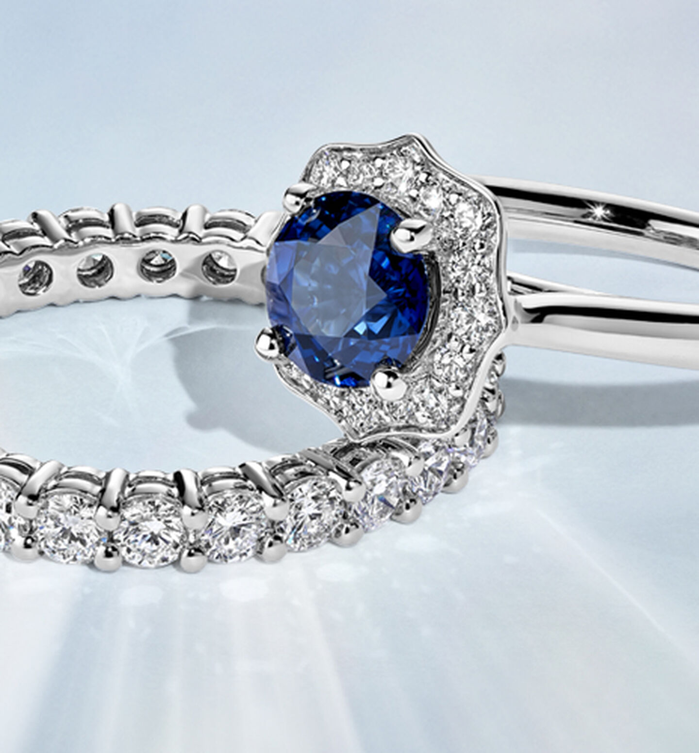 A Birks 1879 Sapphire Engagement Ring stacked on an eternity band on a blue background.