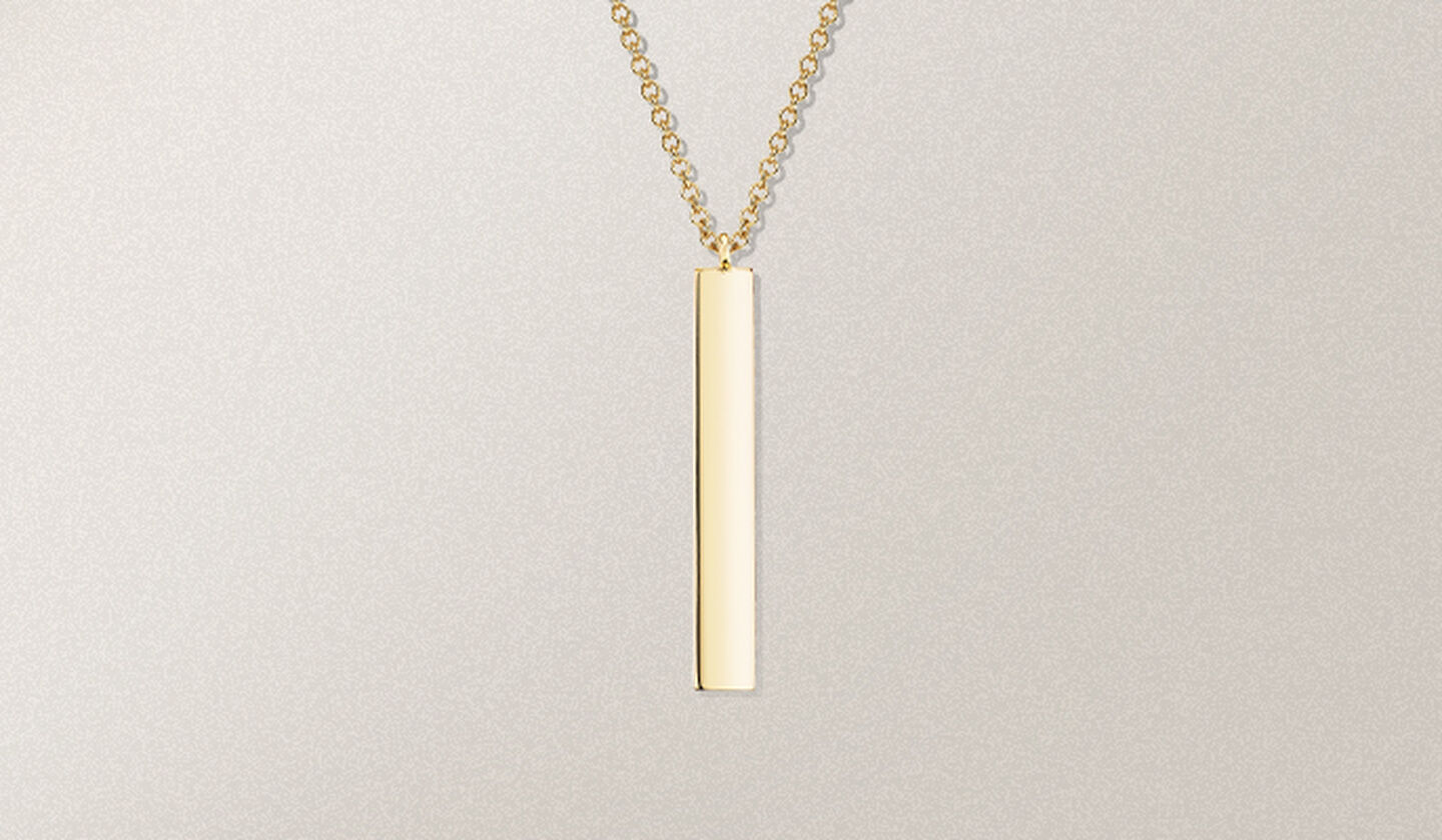 Un collier barre en or jaune de la collection Birks Essentiels sur un fond beige.