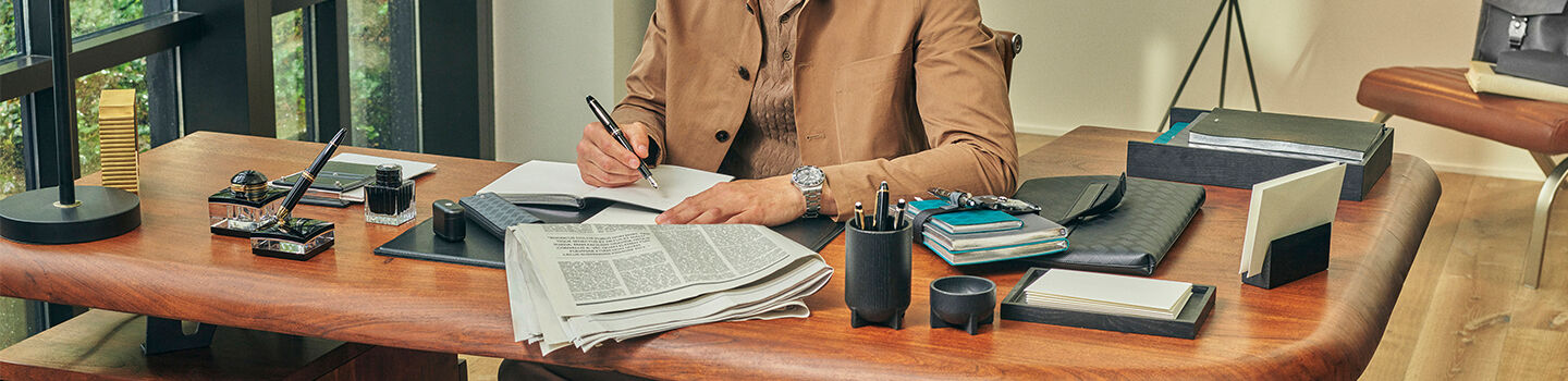 Un homme à son bureau avec des accessoires Montblanc et une montre au poignet.