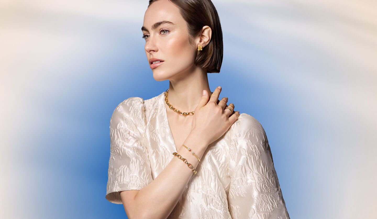 A woman wearing Birks and Roberto Coin jewellery on a blue background.