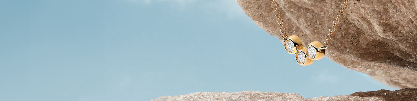 Birks Iconic trio diamond pendant on a brown rock mountain and blue sky background.