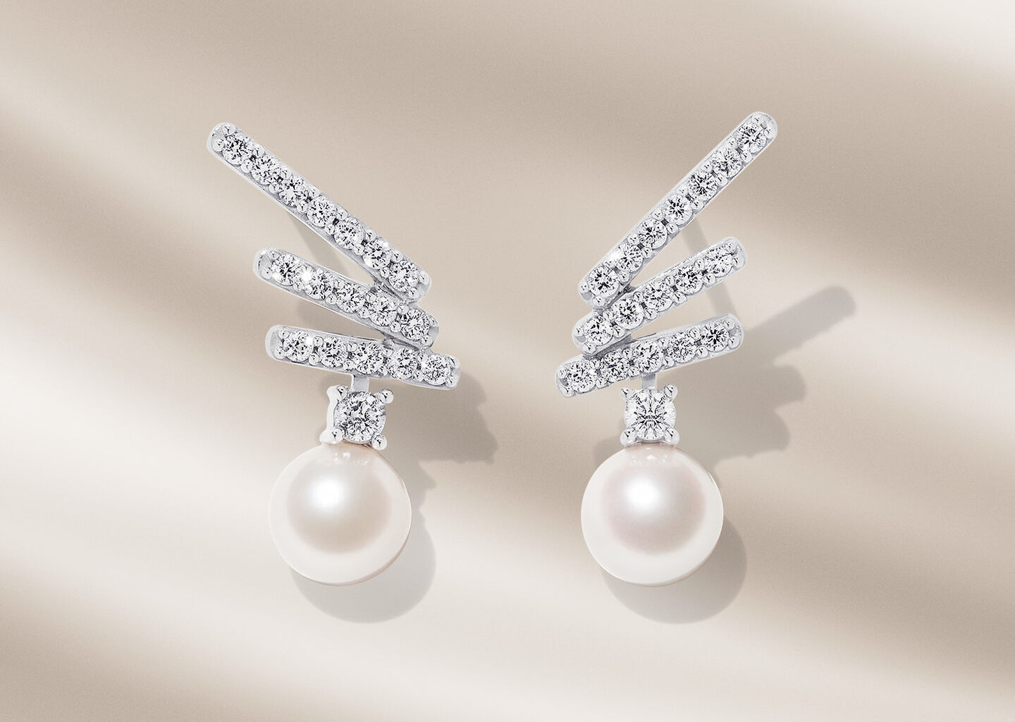 Yoko London diamond and pearl earrings on a beige background.